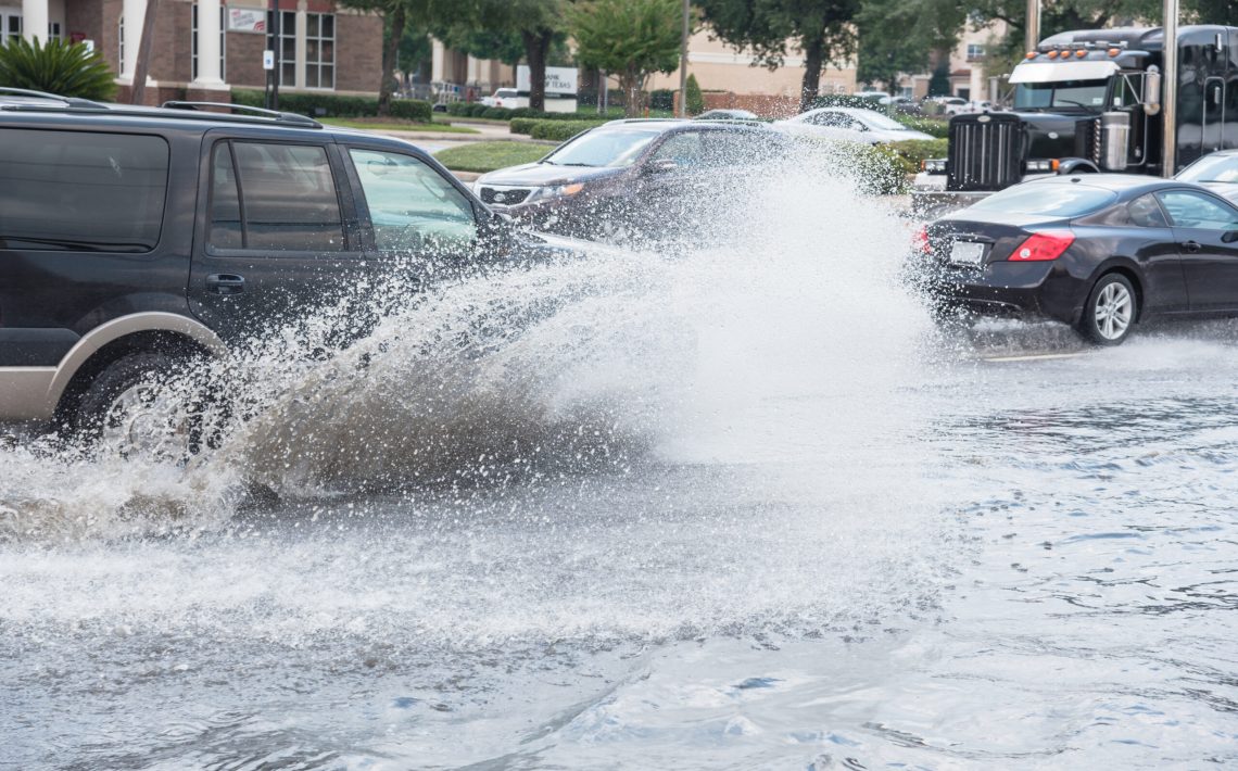Splash by car as it goes through flood water after heavy rains of Harvey hurricane storm in Houston, Texas, US. Flooded city road with big puddle of water spray from the wheels of SUV car roaring by.